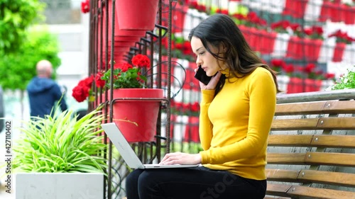 Young woman working with a computer and talking on the phone in a colorful square, full of flowers.