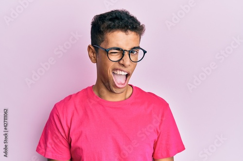 Young handsome african american man wearing glasses over pink background winking looking at the camera with sexy expression, cheerful and happy face. © Krakenimages.com