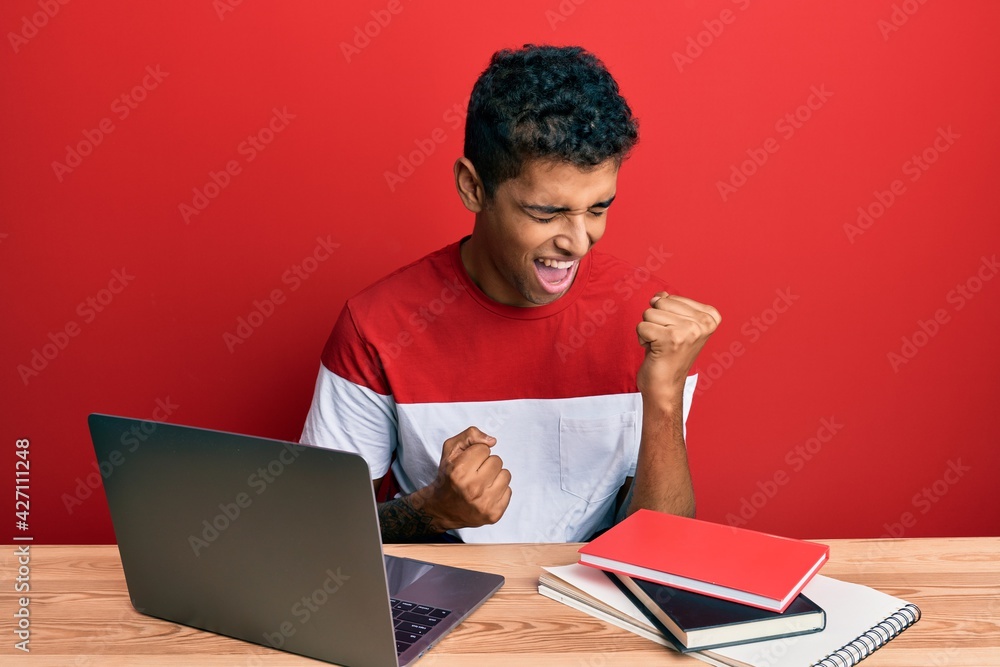 Young handsome african american man studying for school using laptop celebrating surprised and amazed for success with arms raised and eyes closed Young handsome african american man studying for school using laptop celebrating surprised and amazed for success with arms raised and eyes closed