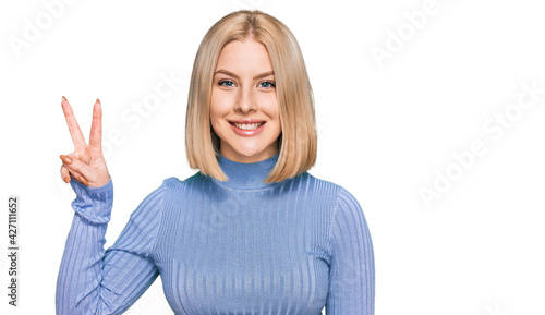Young blonde woman wearing casual clothes smiling with happy face winking at the camera doing victory sign. number two.