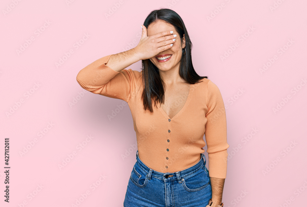 Young hispanic woman wearing casual clothes smiling and laughing with hand on face covering eyes for surprise. blind concept. Young hispanic woman wearing casual clothes smiling and laughing with hand on face covering eyes for surprise. blind concept.