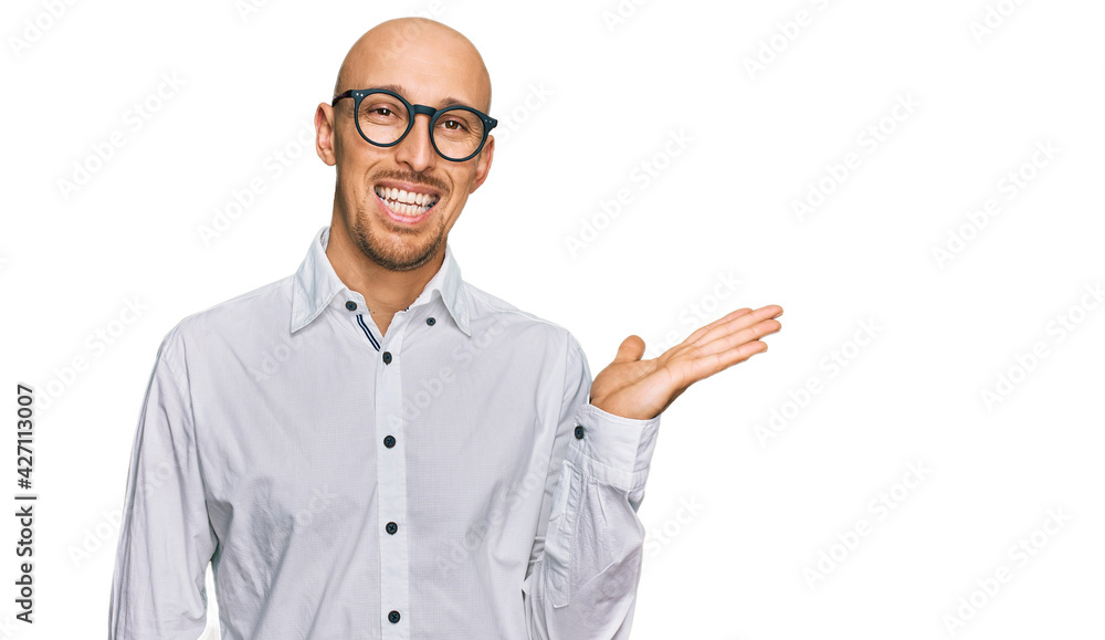 Bald man with beard wearing business shirt and glasses smiling cheerful presenting and pointing with palm of hand looking at the camera. Bald man with beard wearing business shirt and glasses smiling cheerful presenting and pointing with palm of hand looking at the camera.