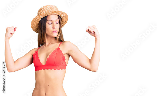 Beautiful brunette young woman wearing bikini showing arms muscles smiling proud. fitness concept.