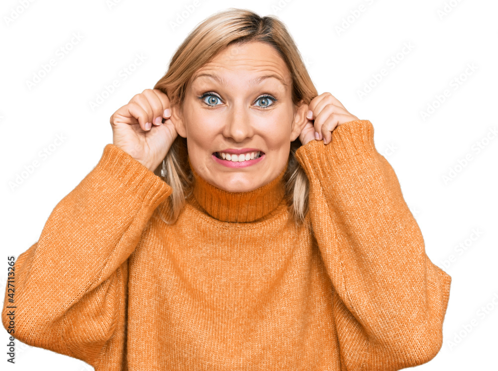 Middle age caucasian woman wearing casual winter sweater smiling pulling ears with fingers, funny gesture. audition problem Middle age caucasian woman wearing casual winter sweater smiling pulling ears with fingers, funny gesture. audition problem