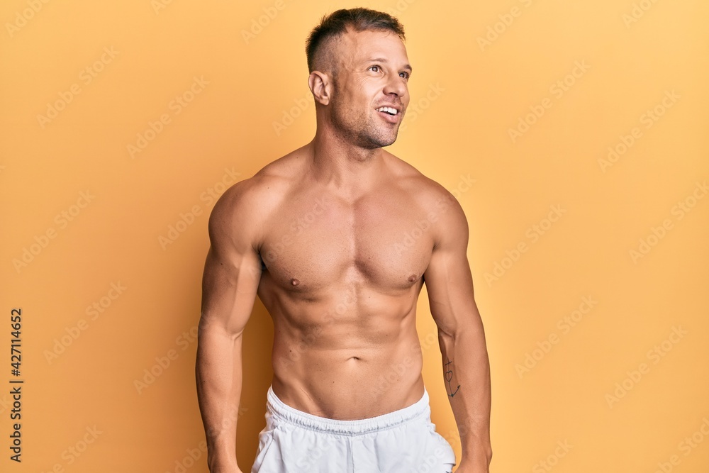 Handsome muscle man standing shirtless looking away to side with smile on face, natural expression. laughing confident.