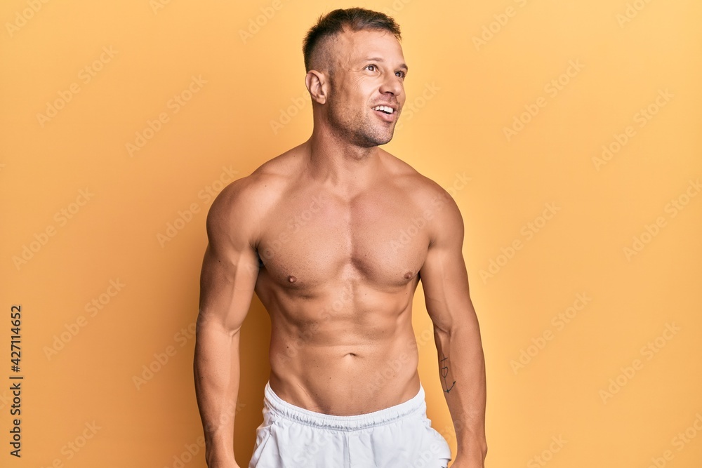 Fototapeta premium Handsome muscle man standing shirtless looking away to side with smile on face, natural expression. laughing confident.