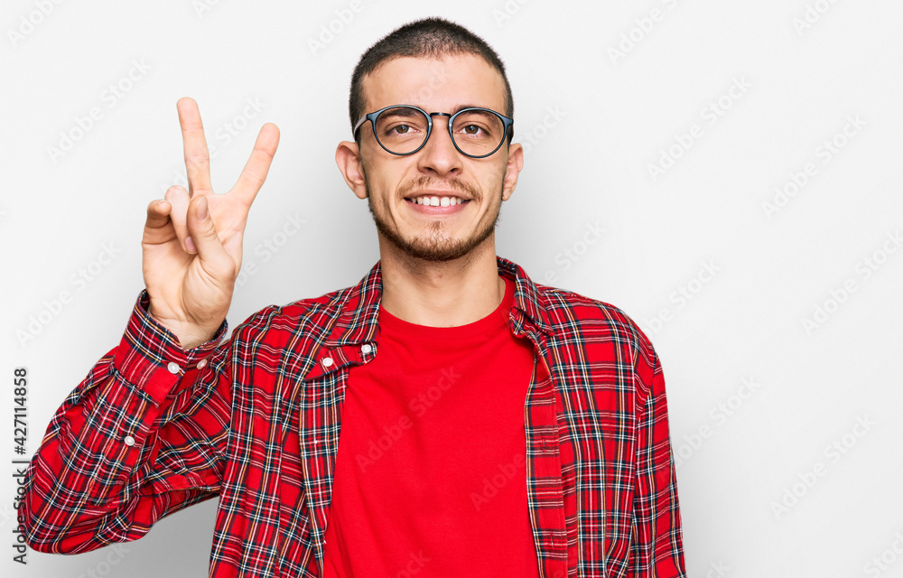 Hispanic young man wearing casual clothes smiling looking to the camera showing fingers doing victory sign. number two. Hispanic young man wearing casual clothes smiling looking to the camera showing fingers doing victory sign. number two.
