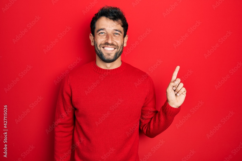 Handsome man with beard wearing casual red sweater with a big smile on face, pointing with hand finger to the side looking at the camera. Handsome man with beard wearing casual red sweater with a big smile on face, pointing with hand finger to the side looking at the camera.
