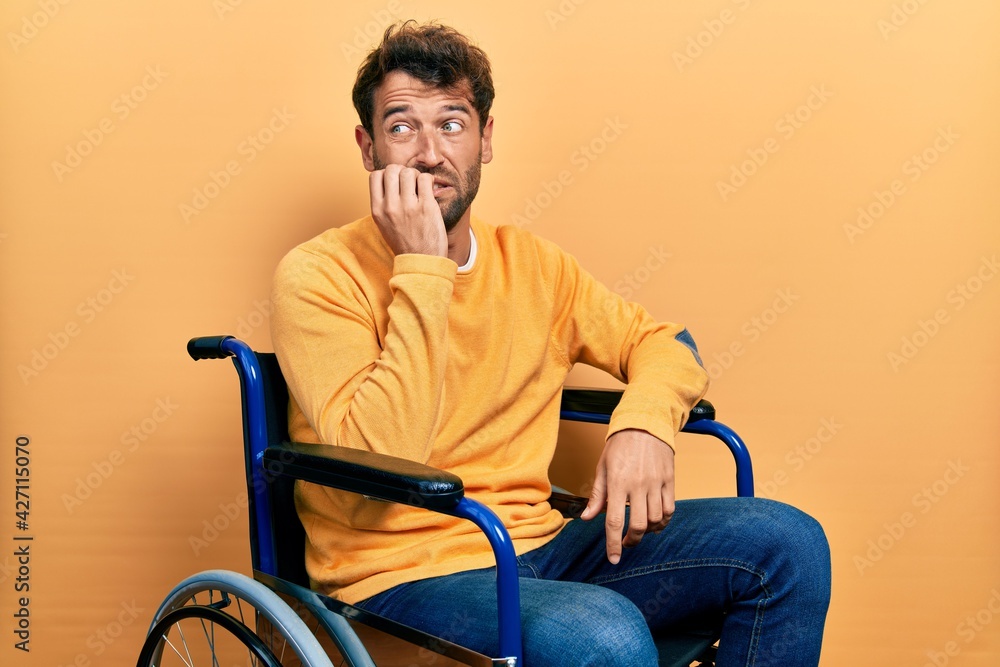 Handsome man with beard sitting on wheelchair looking stressed and nervous with hands on mouth biting nails. anxiety problem.