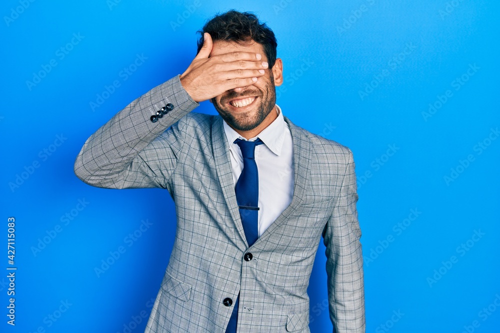 Handsome man with beard wearing business suit and tie smiling and laughing with hand on face covering eyes for surprise. blind concept. Handsome man with beard wearing business suit and tie smiling and laughing with hand on face covering eyes for surprise. blind concept.