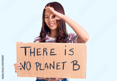Young beautiful chinese girl holding there is no planet b banner smiling happy doing ok sign with hand on eye looking through fingers © Krakenimages.com