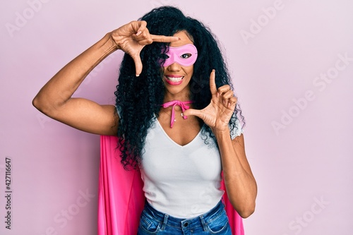 Middle age african american woman wearing super hero costume smiling making frame with hands and fingers with happy face. creativity and photography concept.