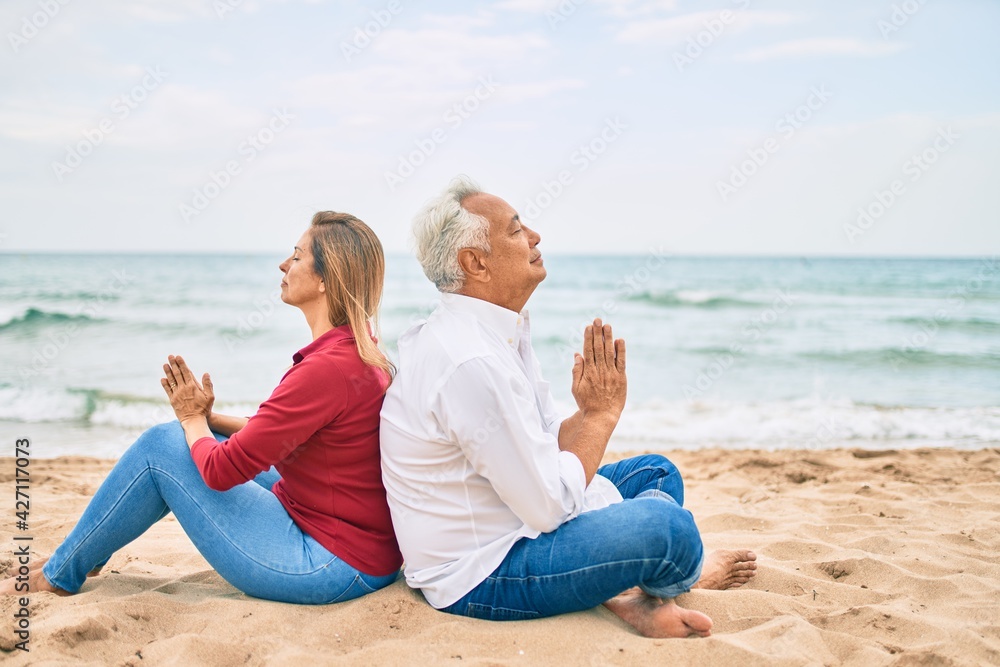 Middle age couple in love doing lotus yoga pose relaxing at the beach happy and cheerful together Middle age couple in love doing lotus yoga pose relaxing at the beach happy and cheerful together