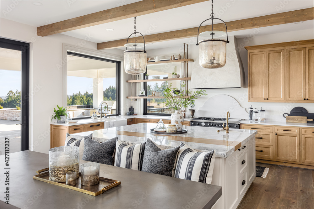 Traditional kitchen in beautiful new luxury home with hardwood floors, wood beams, and large island quartz counters. Includes farmhouse sink, elegant pendant lights, and large windows. - obrazy, fototapety, plakaty 