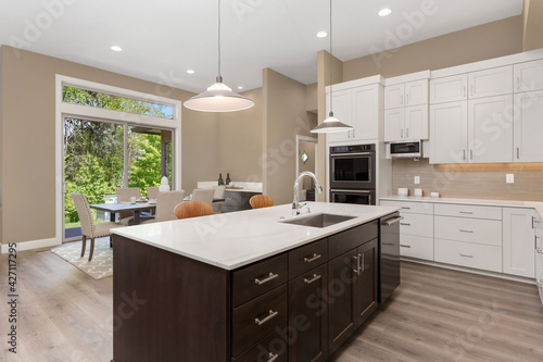 Beautiful kitchen in new luxury home with large island  pendant lights  and stainless steel appliances. Shows eating nook and sliding glass doors leading out to backyard