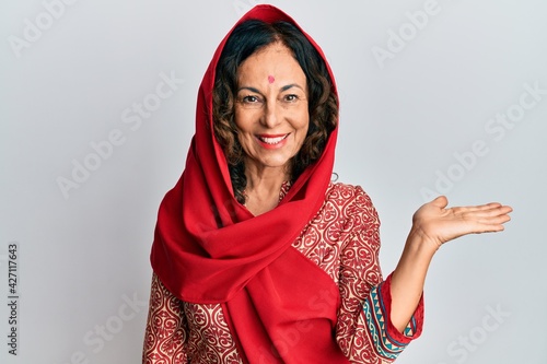 Middle age hispanic woman wearing tradition sherwani saree clothes smiling cheerful presenting and pointing with palm of hand looking at the camera.