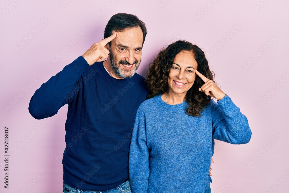 Middle age couple of hispanic woman and man hugging and standing together smiling pointing to head with one finger, great idea or thought, good memory Middle age couple of hispanic woman and man hugging and standing together smiling pointing to head with one finger, great idea or thought, good memory