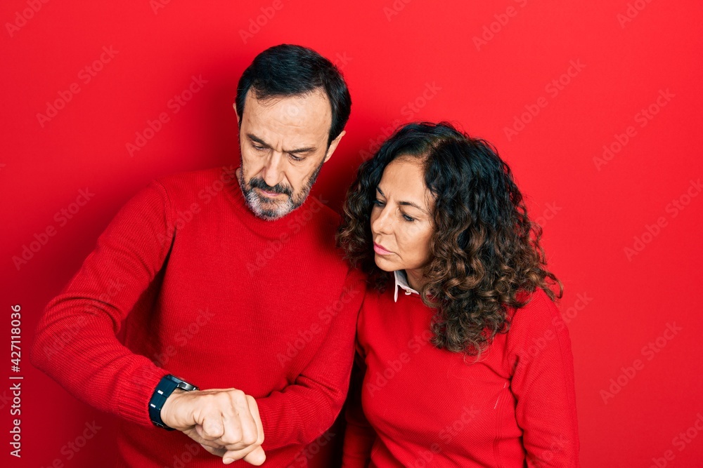 Middle age couple of hispanic woman and man hugging and standing together checking the time on wrist watch, relaxed and confident Middle age couple of hispanic woman and man hugging and standing together checking the time on wrist watch, relaxed and confident