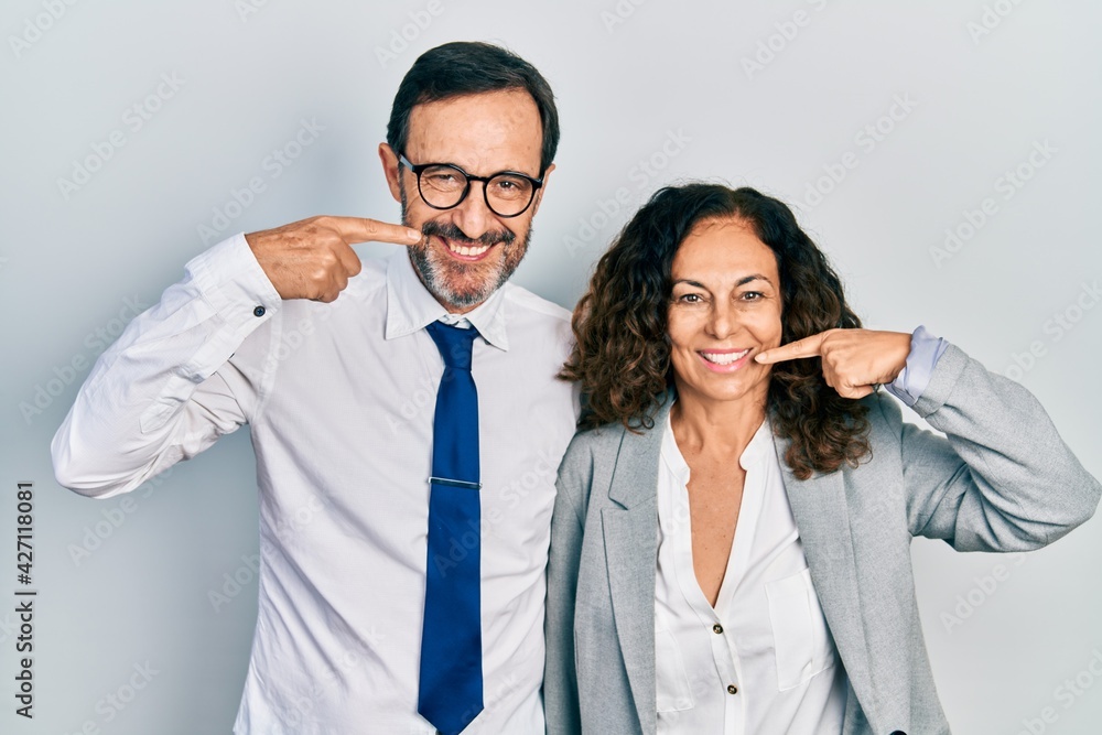 Middle age couple of hispanic woman and man wearing business office uniform smiling cheerful showing and pointing with fingers teeth and mouth. dental health concept. Middle age couple of hispanic woman and man wearing business office uniform smiling cheerful showing and pointing with fingers teeth and mouth. dental health concept.
