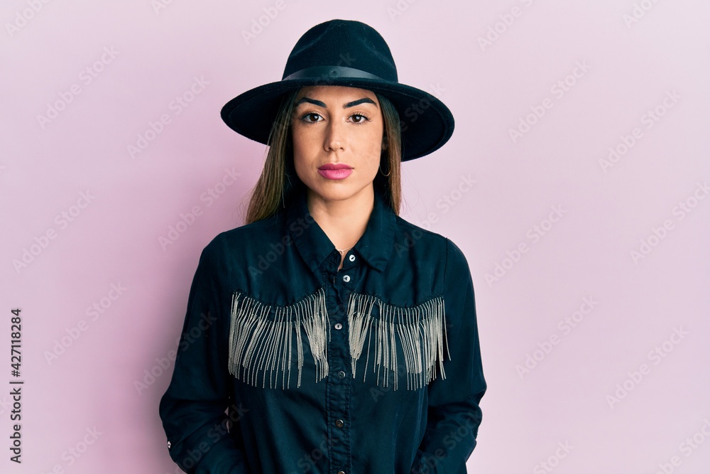 Young hispanic woman wearing cowgirl style with serious expression on face. simple and natural looking at the camera. Young hispanic woman wearing cowgirl style with serious expression on face. simple and natural looking at the camera.