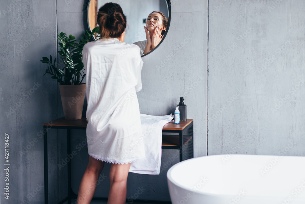 Woman washes in front of the mirror, applying foam to her face Woman washes in front of the mirror, applying foam to her face
