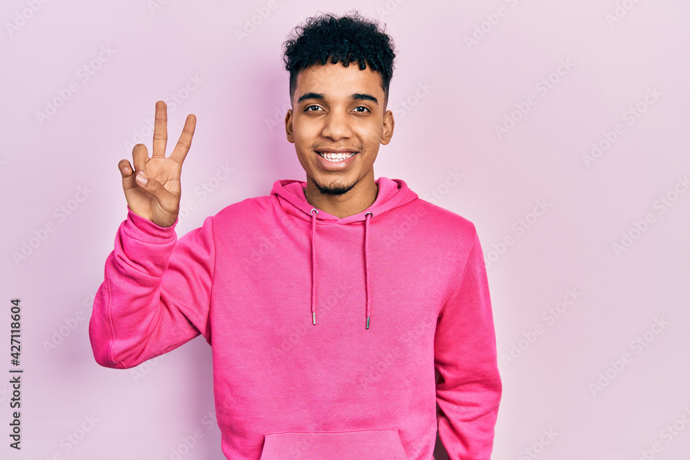 Young african american man wearing casual sweatshirt smiling with happy face winking at the camera doing victory sign. number two. Young african american man wearing casual sweatshirt smiling with happy face winking at the camera doing victory sign. number two.