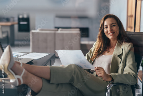 Woman holding a sheet of paper, working at home with her feet on her desk photo