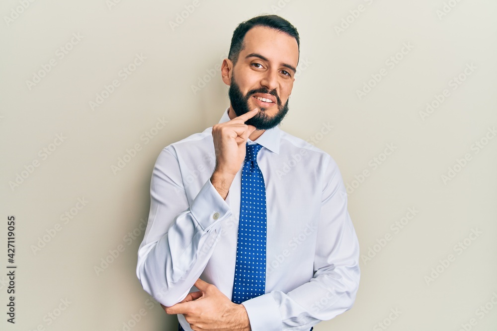 Young man with beard wearing business tie looking confident at the camera with smile with crossed arms and hand raised on chin. thinking positive. Young man with beard wearing business tie looking confident at the camera with smile with crossed arms and hand raised on chin. thinking positive.