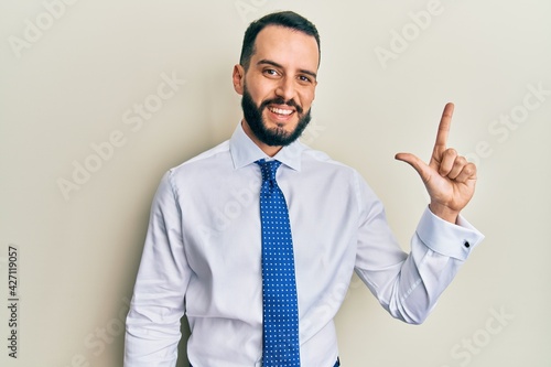 Young man with beard wearing business tie showing and pointing up with fingers number two while smiling confident and happy.