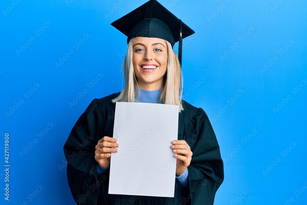 Beautiful blonde woman wearing graduation cap and ceremony robe holding blank banner smiling and laughing hard out loud because funny crazy joke. Beautiful blonde woman wearing graduation cap and ceremony robe holding blank banner smiling and laughing hard out loud because funny crazy joke.