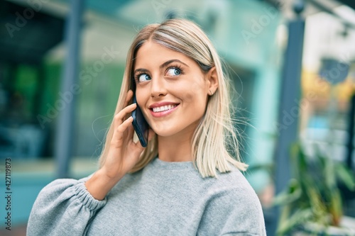 Young blonde girl smiling happy talking on the smartphone at the city
