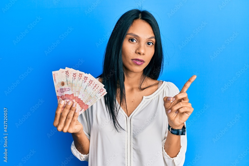 Young african american woman holding 10 colombian pesos banknotes pointing with hand finger to the side showing advertisement, serious and calm face Young african american woman holding 10 colombian pesos banknotes pointing with hand finger to the side showing advertisement, serious and calm face