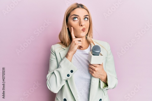 Quadro su tela Young caucasian woman holding reporter microphone serious face thinking about qu