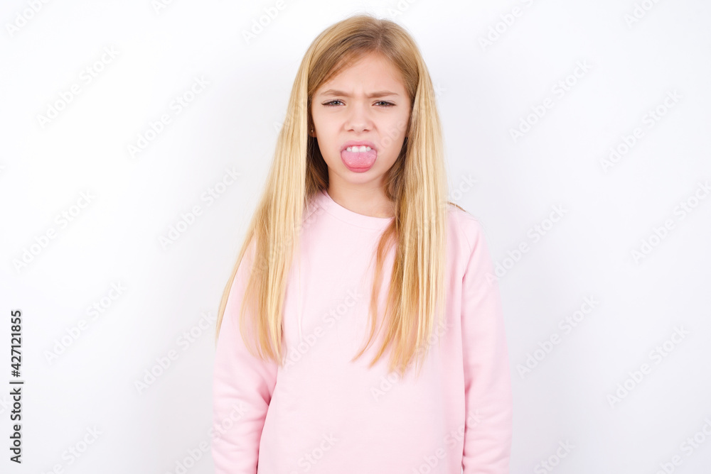 Body language. Disgusted stressed out beautiful caucasian little girl wearing pink hoodie over white background, frowning face, demonstrating aversion to something. Body language. Disgusted stressed out beautiful caucasian little girl wearing pink hoodie over white background, frowning face, demonstrating aversion to something.
