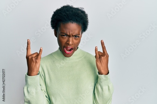 Young african american girl wearing casual clothes shouting with crazy expression doing rock symbol with hands up. music star. heavy concept.