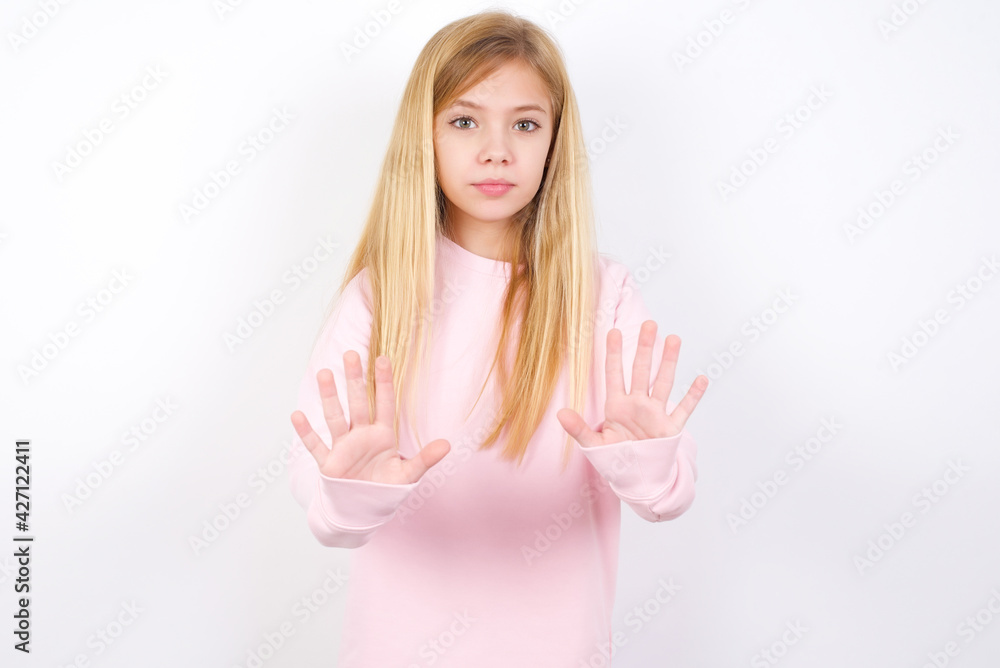 beautiful caucasian little girl wearing pink hoodie over white background doing stop sing with palm of the hand. Warning expression with negative and serious gesture on the face. beautiful caucasian little girl wearing pink hoodie over white background doing stop sing with palm of the hand. Warning expression with negative and serious gesture on the face.
