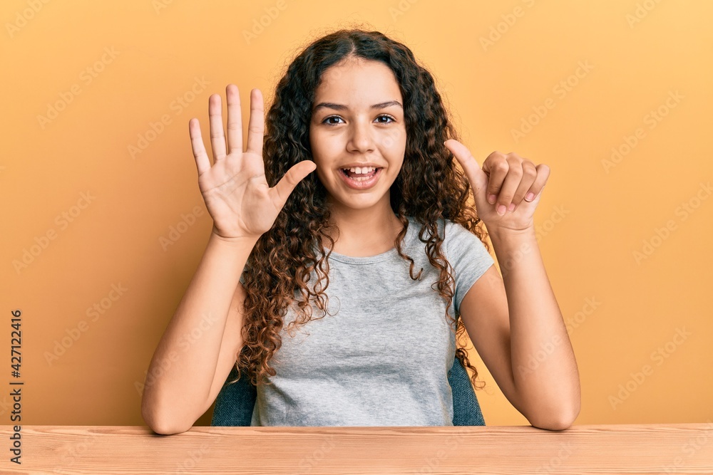 Teenager hispanic girl wearing casual clothes sitting on the table showing and pointing up with fingers number six while smiling confident and happy. Teenager hispanic girl wearing casual clothes sitting on the table showing and pointing up with fingers number six while smiling confident and happy.