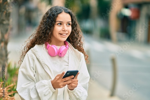 Beautiful hispanic girl smiling happy using smartphone and headphones at the city.