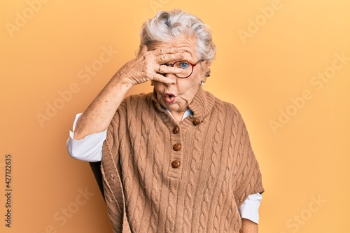 Foto Senior grey-haired woman wearing casual clothes and glasses peeking in shock covering face and eyes with hand, looking through fingers with embarrassed expression