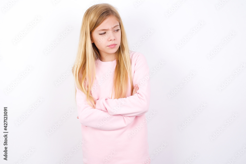Displeased beautiful caucasian little girl wearing pink hoodie over white background with bad attitude, arms crossed looking sideways. Negative human emotion facial expression feelings. Displeased beautiful caucasian little girl wearing pink hoodie over white background with bad attitude, arms crossed looking sideways. Negative human emotion facial expression feelings.
