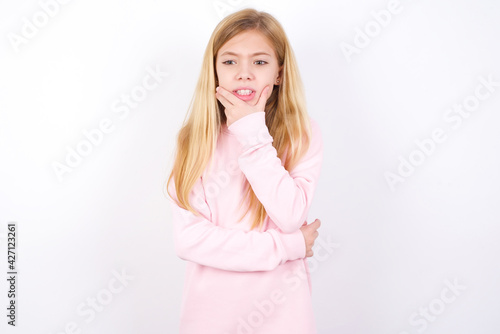 beautiful caucasian little girl wearing pink hoodie over white background covering mouth with hands scared from something or someone bitting nails