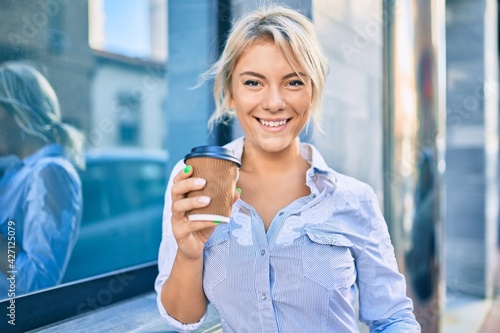 Young blonde woman smiling happy and drinking take away coffee at the city. Free Download Young blonde woman smiling happy and drinking take away coffee at the city. - GFXLoad