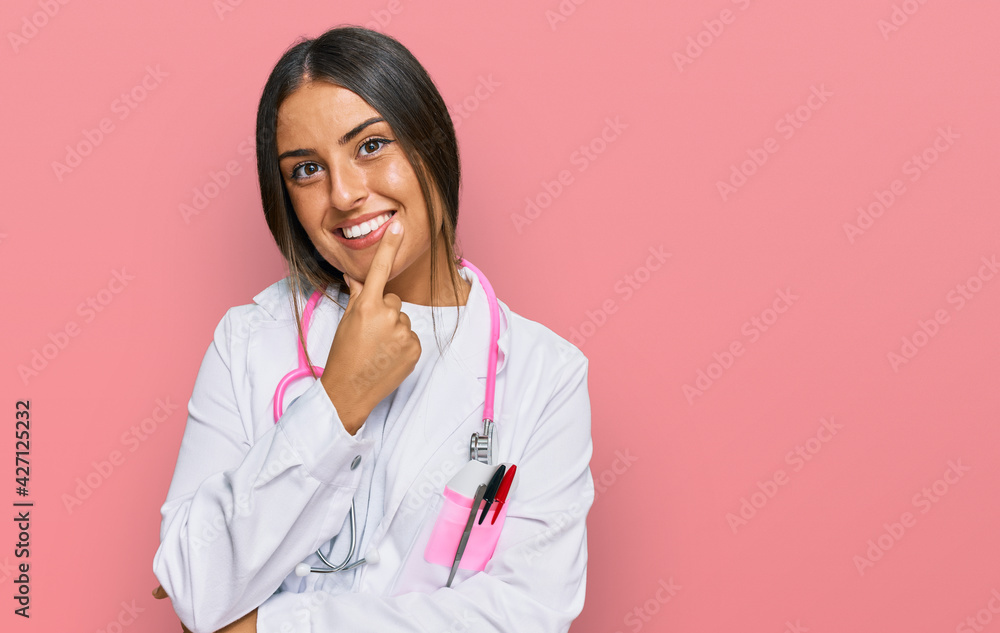Beautiful hispanic woman wearing doctor uniform and stethoscope looking confident at the camera smiling with crossed arms and hand raised on chin. thinking positive. Beautiful hispanic woman wearing doctor uniform and stethoscope looking confident at the camera smiling with crossed arms and hand raised on chin. thinking positive.