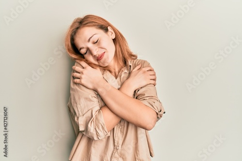 Young caucasian woman wearing casual clothes hugging oneself happy and positive, smiling confident. self love and self care