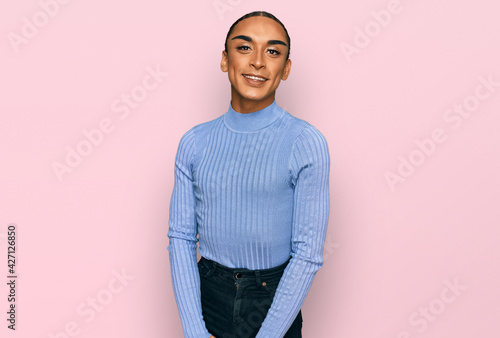 Hispanic transgender man wearing make up and long hair wearing casual clothes looking positive and happy standing and smiling with a confident smile showing teeth photo
