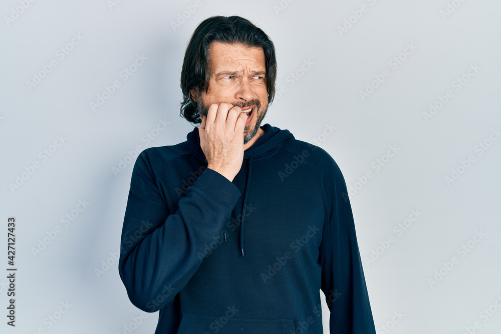 Middle age caucasian man wearing casual sweatshirt looking stressed and nervous with hands on mouth biting nails. anxiety problem. Middle age caucasian man wearing casual sweatshirt looking stressed and nervous with hands on mouth biting nails. anxiety problem.