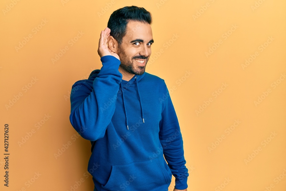 Young hispanic man wearing casual clothes smiling with hand over ear listening an hearing to rumor or gossip. deafness concept.