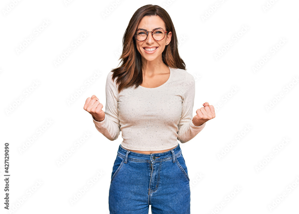 Young brunette woman wearing casual clothes and glasses excited for success with arms raised and eyes closed celebrating victory smiling. winner concept. Young brunette woman wearing casual clothes and glasses excited for success with arms raised and eyes closed celebrating victory smiling. winner concept.