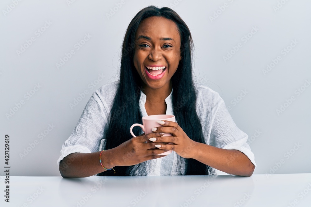 Young african woman drinking a cup coffee celebrating crazy and amazed for success with open eyes screaming excited. Young african woman drinking a cup coffee celebrating crazy and amazed for success with open eyes screaming excited.