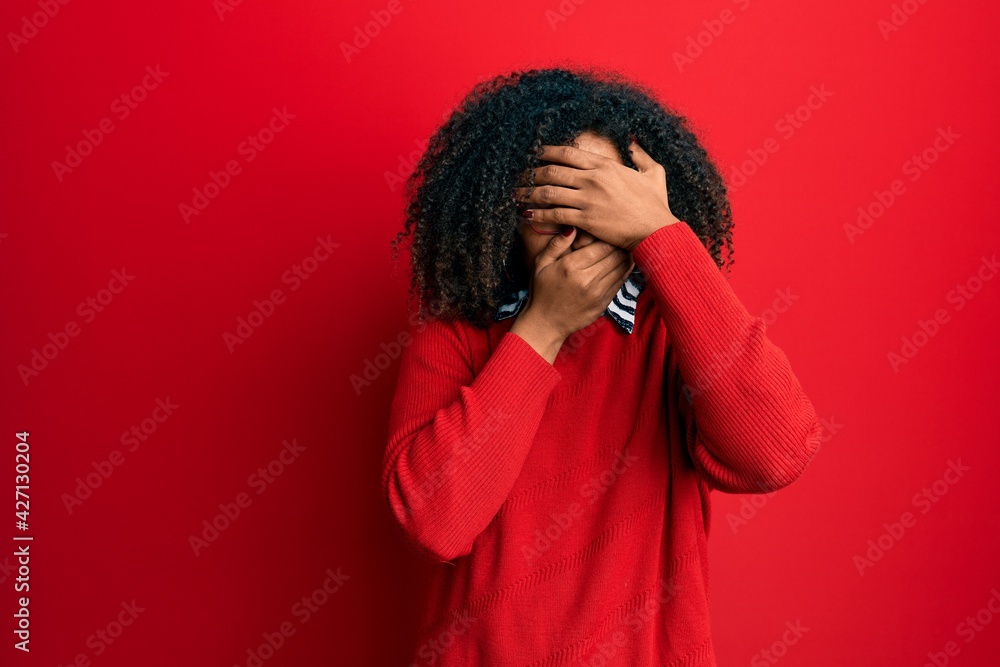 Beautiful african american woman with afro hair wearing sweater and glasses covering eyes and mouth with hands, surprised and shocked. hiding emotion Beautiful african american woman with afro hair wearing sweater and glasses covering eyes and mouth with hands, surprised and shocked. hiding emotion